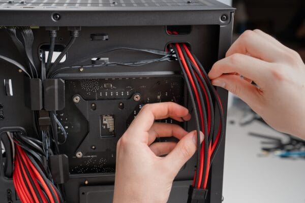 Hender som legger kabler gjennom kabelhull i baksiden av et PC-kabinett under bygging av datamaskin